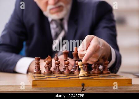 Un vieil employé de sexe masculin joue aux échecs sur le lieu de travail Banque D'Images