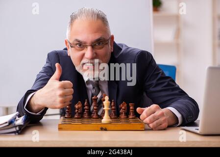 Un vieil employé de sexe masculin joue aux échecs sur le lieu de travail Banque D'Images