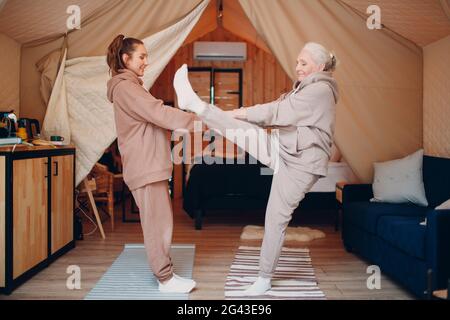 La famille fait des exercices d'échauffement sports à l'intérieur. Jeune et âgée, femme se détendant dans une tente de camping glamping. Mère et d Banque D'Images