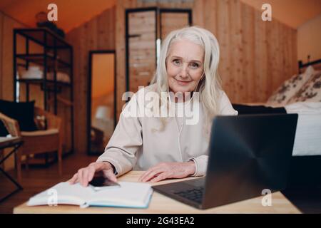 Femme d'âge mûr avec ordinateur portable assis à la table et parlant dans une tente de camping glamping. Concept moderne de mode de vie de vacances. Banque D'Images