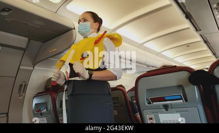 Femme hôtesse de vol sous masque facial présentant la gilet de sauvetage à bord avant le départ du vol Banque D'Images