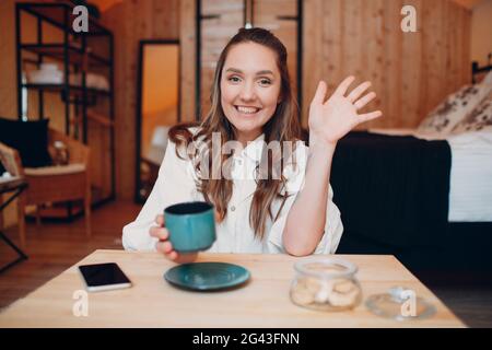 Écran de l'application de la jeune femme souriante s'asseoir à table avec un ordinateur portable et de parler sur appel vidéo avec un ami ou un collègue, happ Banque D'Images