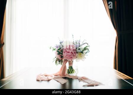 Bouquet de mariée de pivoines blanches et roses, branches d'olive, lavande et campanula avec rubans roses dans le vase en verre sur le tabl Banque D'Images