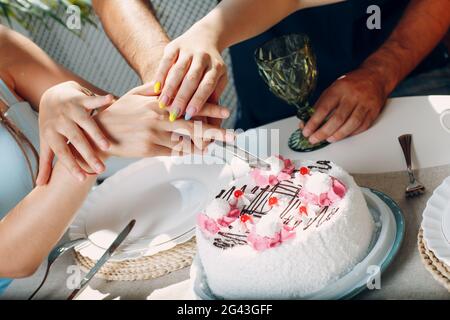 Les mains coupent le gâteau blanc ensemble. Concept « Joyeux anniversaire ». Banque D'Images