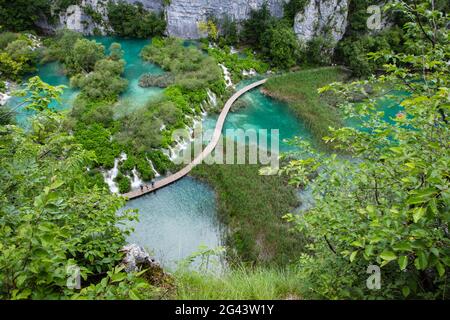 Vue sur les gens sur le chemin de bois en bois au-dessus de la piscine avec des cascades, Parc national des lacs de Plitvice, Lika-Senj, Croatie, Europe Banque D'Images