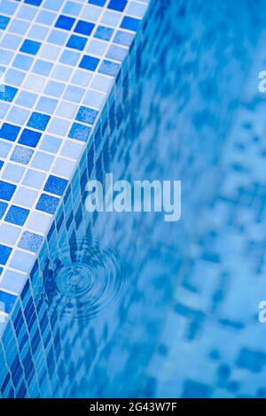 Taches d'eau d'une goutte aux marches avec une mosaïque bleue dans la piscine. Banque D'Images