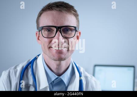 Portrait d'un beau médecin de famille adulte au bureau médical. Médecin réussi en blouse de laboratoire blanche regardant la caméra et souriant Banque D'Images
