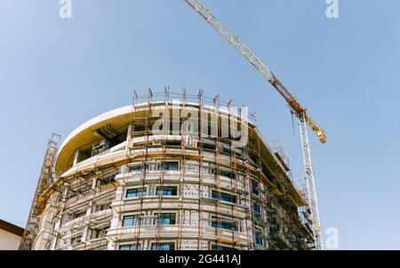 Échafaudage en construction autour d'un bâtiment moderne de plusieurs étages. Il y a une grue de construction sur le toit Banque D'Images