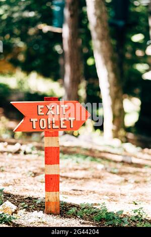 Un panneau rouge avec une inscription sur une colonne à rayures blanches se dresse sur la pelouse de la forêt. Titre : toilettes de sortie Banque D'Images