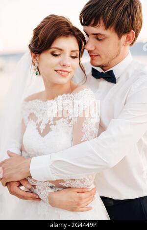 Le marié encadre doucement la mariée de derrière Banque D'Images
