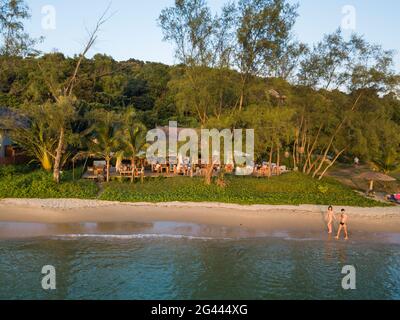 Vue aérienne d'un jeune couple marchant le long de la plage d'Ong Lang avec le restaurant et le bar de Mango Bay Resort derrière, Ong Lang, Phu Quoc Island, Kien Giang Banque D'Images