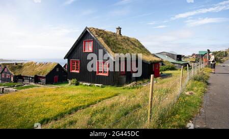 Maisons noires avec des fenêtres rouges et un toit en herbe dans le village de Kirkjubøur sur Streymoy au soleil, îles Féroé Banque D'Images