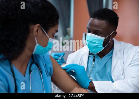 Race mixte couple de médecins portant des masques faciaux faisant l'injection Banque D'Images