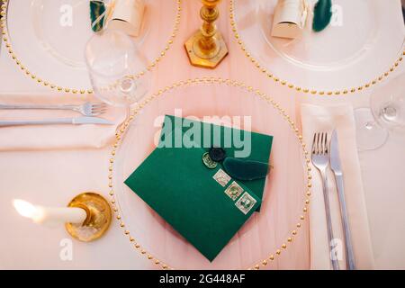 Les enveloppes vierges vertes avec des tampons sont placées sur une plaque transparente d'une table fixe. Une bougie allumée est allumée sur la gauche. Vue de dessus Banque D'Images