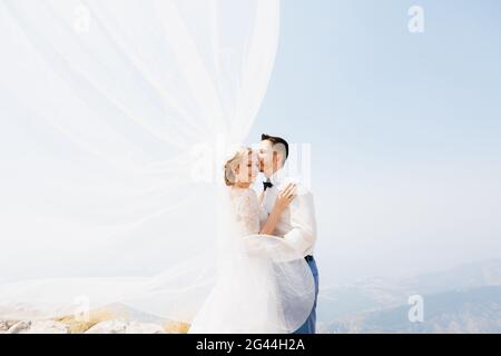 La mariée et le marié embrassent la montagne, le marié embrasse la mariée, le vent fait le voile Banque D'Images