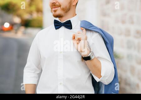 Un homme se tient devant une maison en briques blanches Dans la vieille ville de Perast et tient une veste sur son épaule Banque D'Images