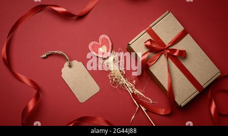 Boîte rectangulaire en carton brun attaché avec un ruban rouge de soie sur un fond rouge, Banque D'Images