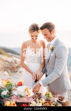 La mariée et le marié coupent un gâteau pendant un Table de buffet après la cérémonie de mariage sur le Mont Lovcen et sourire Banque D'Images