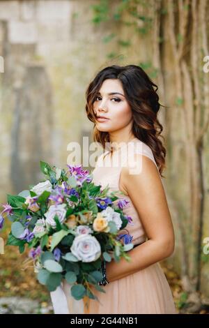 Belle mariée dans une robe crème avec un bouquet de roses entre ses mains Banque D'Images