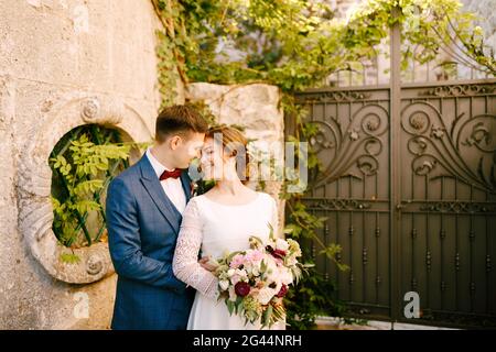 Mariée souriante et marié embrassant sur le fond de corroyé portes en fer dans le jardin Banque D'Images