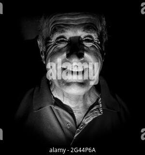 Portrait of smiling old man. Tourné en noir et blanc, éclairage discret. Isolé sur le noir. Banque D'Images