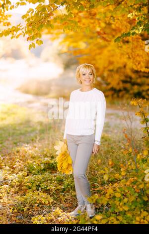 Femme souriante debout avec bouquet de feuilles jaunes en automne forêt Banque D'Images