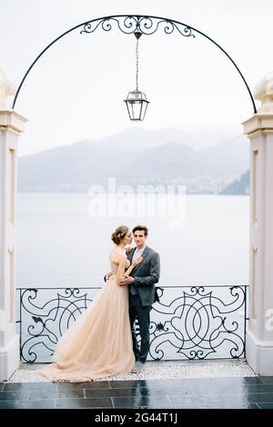 Les newlyweds se ruent et s'embrassent presque sous une vieille arche contre La toile de fond du lac de Côme Banque D'Images