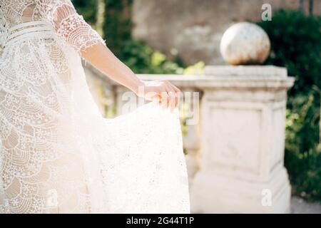 Mariée tient avec ses doigts le plancher d'un blanc robe de mariage en dentelle sur le fond des colonnes dans le jardin Banque D'Images