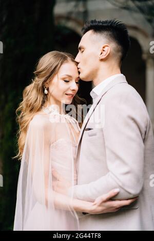 Le marié embrasse le front de la mariée souriante dans une belle robe rose Banque D'Images