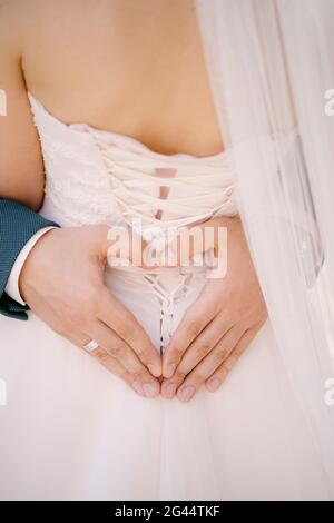 Le marié tient ses mains en forme de cœur sur le dos de la mariée dans une robe blanche Banque D'Images