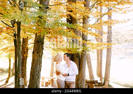 Homme et femme en chandail blanc qui s'embrasse sur un fond de feuilles jaunes et rouges dans la forêt d'automne Banque D'Images