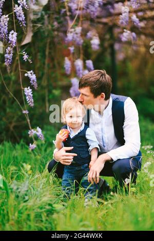 Le père embrasse son bébé garçon sur le dessus de la tête avec une wysteria fleurir en arrière-plan Banque D'Images