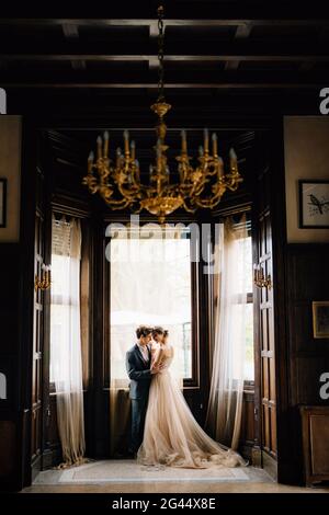 Le marié hantit mariée sur le fond des grandes fenêtres de la vieille villa. Vue de la chambre d'à côté avec un lustre avec ca Banque D'Images