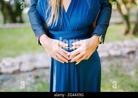 Les mains de l'homme se câblent de derrière le ventre de la femme enceinte dans une robe bleue Banque D'Images