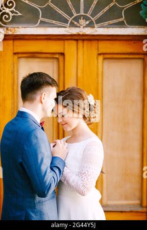 Le marié embrasse une belle mariée souriante sur le fond de la porte jaune vitrée. Le marié tient les mains de la mariée Banque D'Images