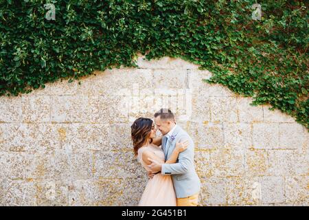 Marié embrasse la mariée avec tendresse embrassant sur le fond de un mur de pierre enmêché de lierre verte Banque D'Images