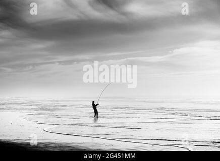 Silhouette de pêcheur pêche sur la plage en noir et blanc Banque D'Images