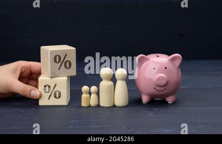 Figurines de famille en bois et banc de porc en céramique rose sur fond bleu, concept de sauvegarde Banque D'Images