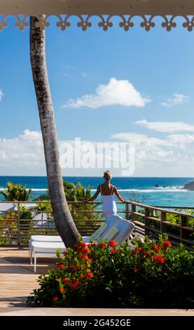 Femme en blanc, debout sur une terrasse avec son dos à la caméra, en regardant sur l'océan. Saint-Barths. Banque D'Images