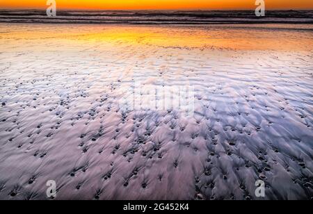 Galets dans le sable sur la plage de l'océan Pacifique au coucher du soleil Banque D'Images