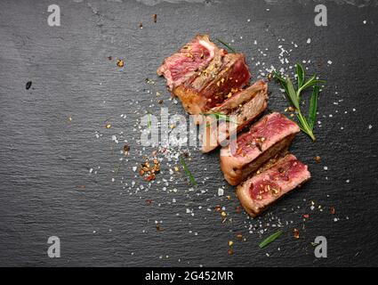 Steak de bœuf frit en tranches de New York striploin sur fond noir avec épices, degré de donaité rare Banque D'Images