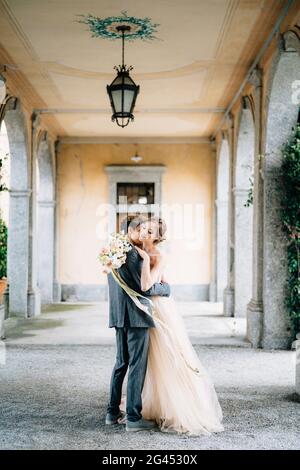 Marié câlins et baisers mariée avec un bouquet de fleurs sur une vieille terrasse avec des colonnes enremplies de lierre verte. Lac de Côme Banque D'Images