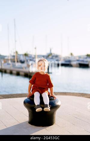 Un portrait d'une jolie fille de 2 ans assise sur une jetée de bateau au bord de la mer Banque D'Images