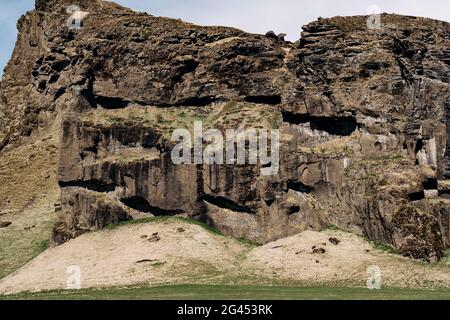 Un pré vert, un terrain pour le pâturage des bovins avec de l'herbe, sur fond de montagnes rocheuses et de ciel bleu avec des nuages blancs dedans Banque D'Images