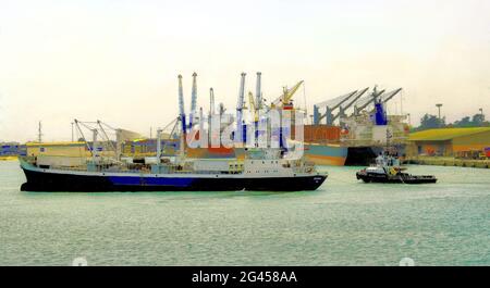 Un navire de mer entrant dans le port de Cotonou, au Bénin, en Afrique de l'Ouest par un jour de brume avec l'aide d'un remorqueur, tandis que d'autres navires sont déjà amarrés. Banque D'Images