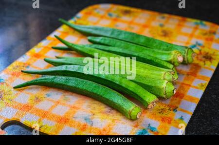 Mise au point sélective de quelques gousses d'okra placées sur une planche à découper en plastique. Arrière-plan en granit noir. Banque D'Images