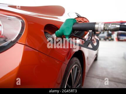 Buse de pompe à gaz benzène verte pour remplir le réservoir de voiture sport rouge. Gros plan Banque D'Images