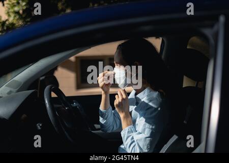 Femme caucasienne assise dans une voiture portant le masque de covid19 du coronavirus Banque D'Images