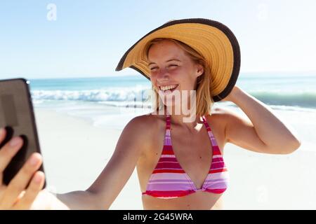 Femme caucasienne à la plage portant un chapeau et prenant selfie avec son smartphone Banque D'Images