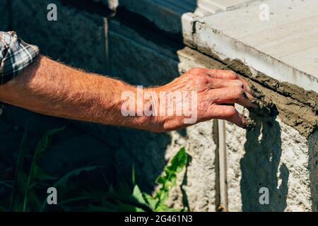 Une vieille couche de briques pose des carreaux de béton à l'extérieur pendant une journée d'été. Main mâle avec mortier de ciment gros plan. Banque D'Images